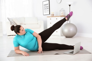 Overweight woman doing exercise while watching tutorial on laptop at home