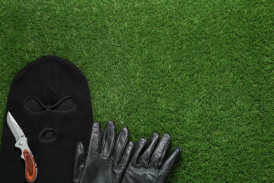 Photo of Black knitted balaclava, gloves and knife on green grass, flat lay. Space for text