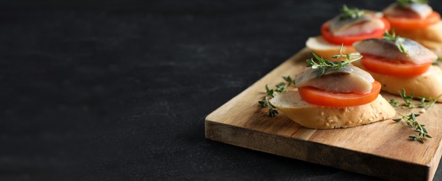 Image of Delicious sandwiches with salted herring, tomato and thyme on black table, closeup view with space for text. Banner design