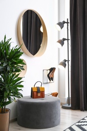 Hallway interior with big round mirror and ottoman chair near white wall