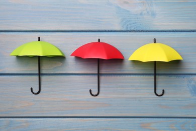Small color umbrellas on light blue wooden background, flat lay