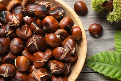Delicious roasted edible chestnuts on brown wooden table, flat lay