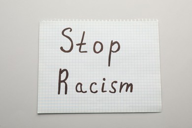 Paper sheet with phrase Stop Racism on light table, top view