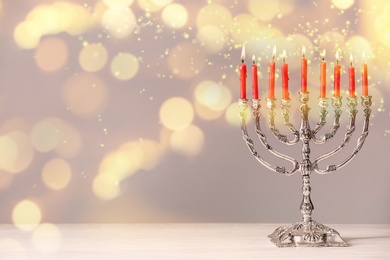 Silver menorah with burning candles on table against light background, space for text. Hanukkah celebration