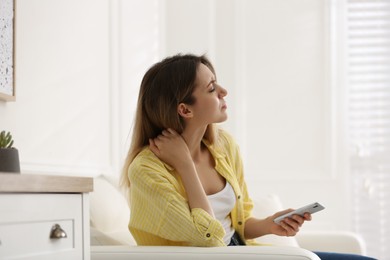 Photo of Woman with smartphone suffering from neck pain at home. Symptom of bad posture