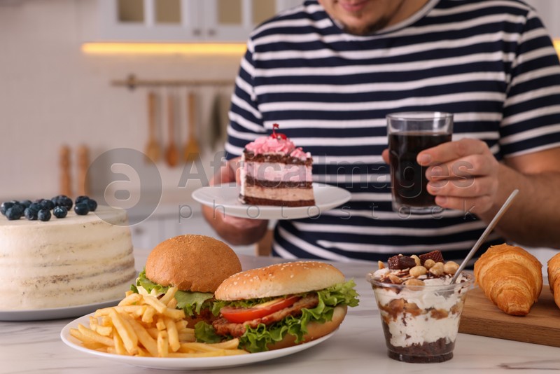 Overweight man with glass of cold drink and cake at table in kitchen, closeup