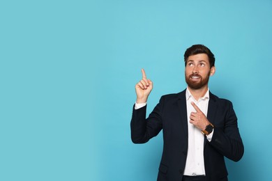 Smiling bearded man pointing index fingers up on light blue background. Space for text