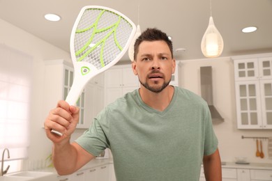 Man with electric fly swatter in kitchen. Insect killer