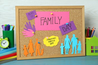 Cork board with text International Family Day and paper cutouts on light blue wooden table