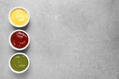 Set of different delicious sauces on grey table, top view. Space for text