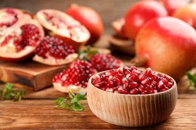 Delicious ripe pomegranate kernels in bowl on wooden table