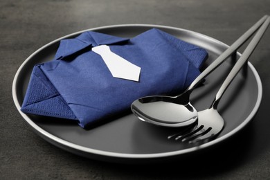 Photo of Plate with shirt made of paper napkin and cutlery on grey table, closeup. Business lunch concept