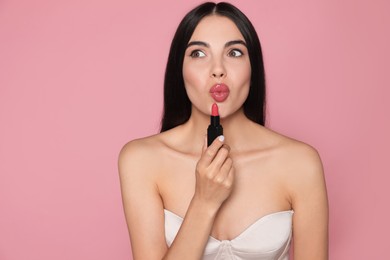 Photo of Emotional young woman with beautiful makeup holding glossy lipstick on pink background