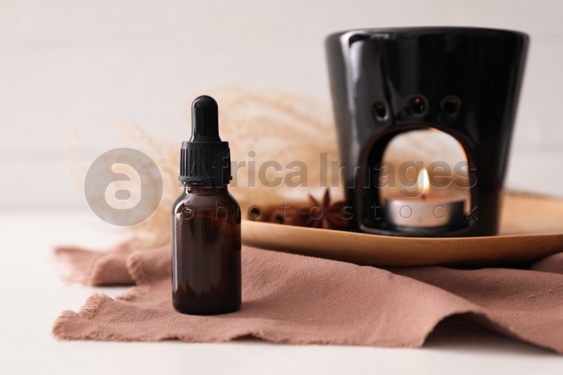 Aroma lamp and cinnamon essential oil on white table, space for text