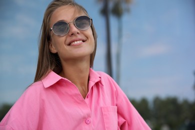 Photo of Portrait of beautiful young woman in stylish sunglasses near building outdoors, space for text
