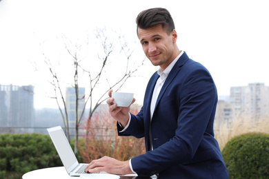 Photo of Businessman with laptop and coffee in outdoor cafe. Corporate blog