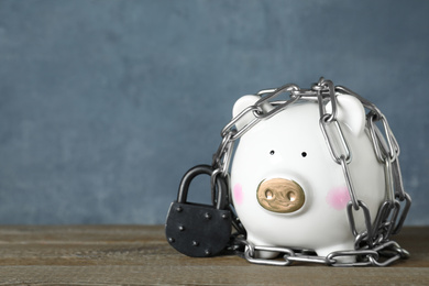 Piggy bank with steel chain, padlock on wooden table, space for text. Money safety concept