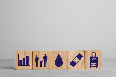 Wooden cubes with different icons on light grey table, space for text. Insurance concept