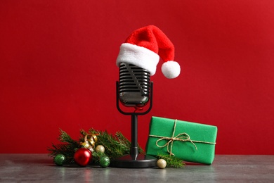 Microphone with Santa hat and decorations on grey table against red background. Christmas music