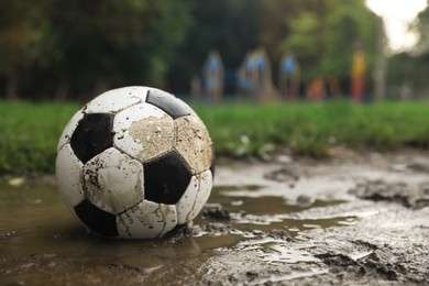 Photo of Dirty leather soccer ball in puddle outdoors, space for text