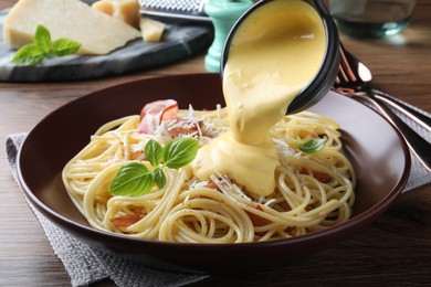 Pouring tasty cheese sauce onto spaghetti with meat on wooden table, closeup