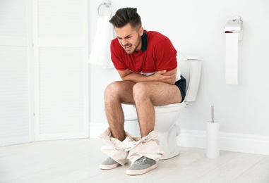 Young man suffering from diarrhea on toilet bowl at home