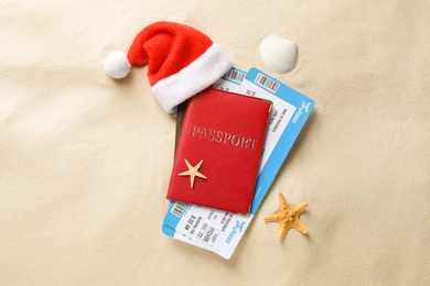 Passport with tickets and Santa hat, seashell, starfish on sand, flat lay. Christmas vacation