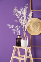 Photo of Stylish vases with beautiful branches near purple wall