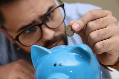 Young man putting coin into piggy bank, focus on hand. Money savings