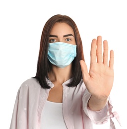 Young woman in protective mask showing stop gesture on white background. Prevent spreading of coronavirus