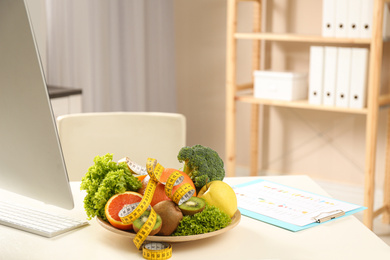 Nutritionist's workplace with fruits, vegetables and measuring tape on table