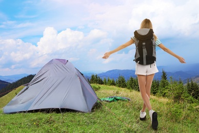 Tourist with travel backpack near camp tent in mountains. Summer vacation trip