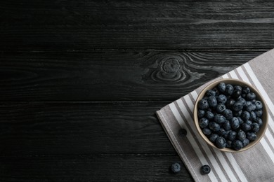 Ceramic bowl with blueberries on black wooden table, flat lay and space for text. Cooking utensil