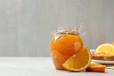 Delicious orange marmalade in glass jar on light grey table. Space for text
