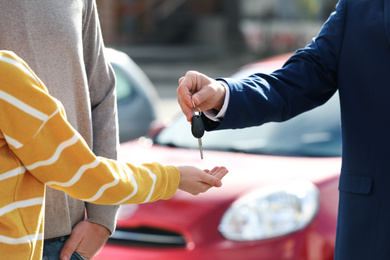 Salesman giving key to customers in modern auto dealership, closeup. Buying new car