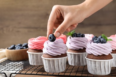 Woman decorating cupcake with fresh blueberry at wooden table, closeup
