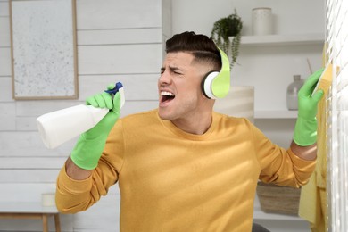 Photo of Man with spray bottle and sponge singing while cleaning at home