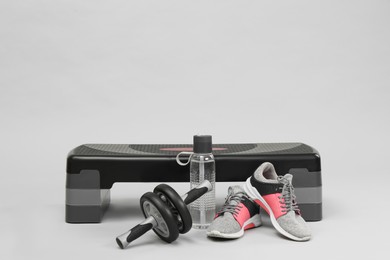 Step platform, abdominal wheel, water bottle and sneakers on light background, space for text. Sport equipment