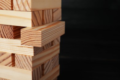 Jenga tower made of wooden blocks on black background, closeup. Space for text