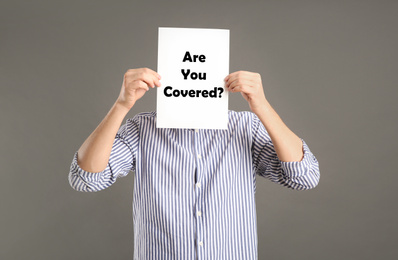 Man holding paper with text ARE YOU COVERED? on grey background. Insurance concept