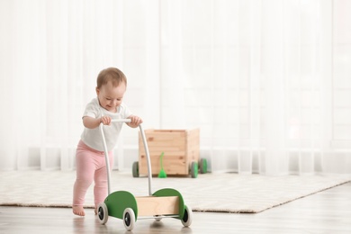 Photo of Cute baby with toy walker at home