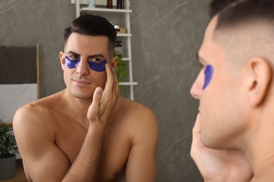 Man applying blue under eye patches near mirror at home