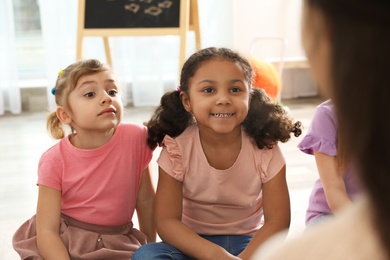 Cute little children listening to teacher indoors. Kindergarten playtime activities