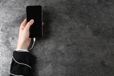 Man holding smartphone in hand tied with charging cable at grey table, top view and space for text. Internet addiction
