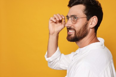 Profile portrait of smiling bearded man with glasses on orange background. Space for text