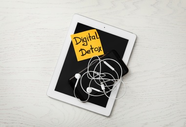 Photo of Different gadgets and sticking paper with words DIGITAL DETOX on white wooden background, top view