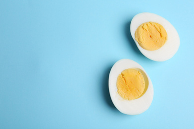 Halves of fresh hard boiled chicken egg on light blue background, flat lay. Space for text