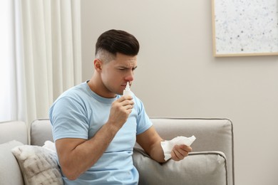 Ill man with paper tissue using nasal spray on sofa at home