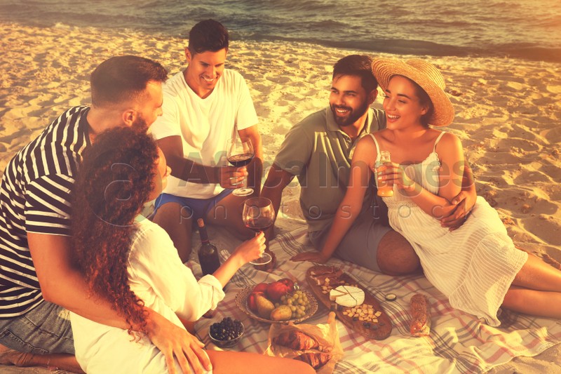 Group of friends having picnic on sandy beach near sea