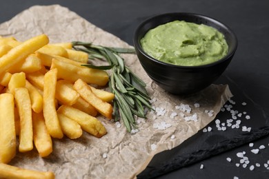Serving board with french fries, guacamole dip and rosemary on black table, closeup